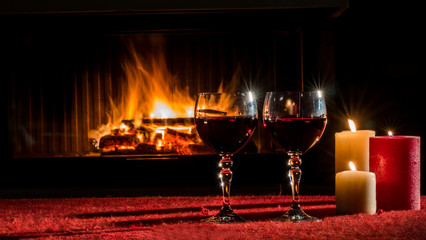 Two glasses with red wine against the background of the fireplace where the fire is burning