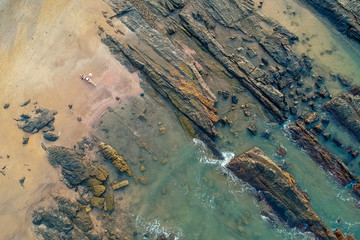 Young woman in a bikini and pareo with long train lying on the back on the sand near the waves of blue sea. Top view