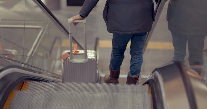 A man with a suitcase on wheels descends down an escalator in a building