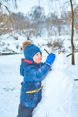 Fototapeta na wymiar little boy in a hat and mittens makes a snowman in winter