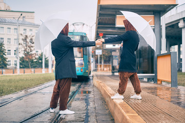 man and woman hold hands. young couple at a bus stop in the rain with an umbrella