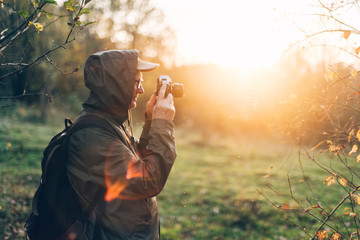 Handsome senior man photographer standing in autumn park and taking pictures with camera.