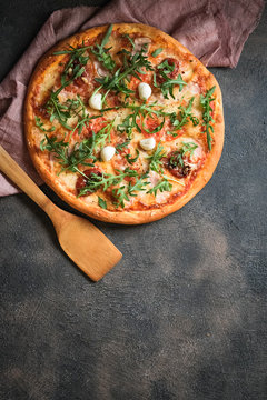 Traditional Italian pizza with ham, mushrooms, arugula, mozzarella, basil and tomatoes on a dark background top view copy space.