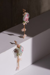 Close-up shot of golden earrings made as crystals with pendants in the form of colorful exotic flowers, gems and golden chains with pink chiffon flowers isolated on the white block in shadows. 