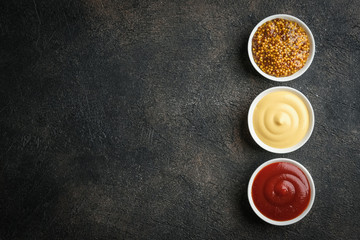 Obraz na płótnie Canvas Set of popular sauces - mustard, ketchup and mayonnaise on a dark background. Top view free copy space.