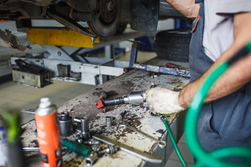Car repair in the service station. Hands of a mechanic in overalls repairing the car on the lift without wheel, holding the tire and mechanical works.