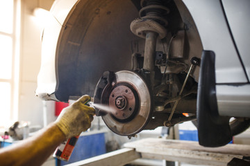 Car repair in the service station. Hands of a mechanic in overalls repairing the car on the lift without wheel, holding the tire and mechanical works.