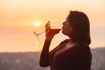 Woman with red wine on sunset mountains, close up of hand holding glass of wine. Elegant woman...