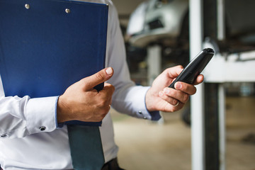 The hand of the master of the inspector in the service station in a white shirt with a tablet for recording. Record of cars for repair in service, work process.