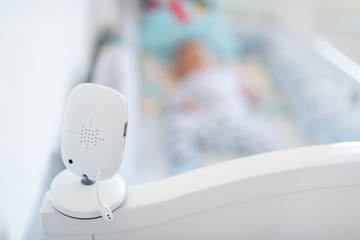 Close up of modern baby monitor on crib. In background is blurred baby boy.