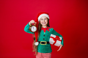 Merry Christmas, happy attractive girl with a clock and gifts in the costume of Santa Claus helper on a bright red bright color background.