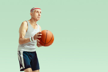 Senior man wearing sportwear playing basketball isolated on green background. Caucasian man in...