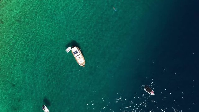 High angle aerial drone footage of boats on a sea close to coast. Pristine  teal, emerald/ turquoise water. Camera is moving up and rotating.
