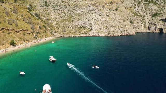 Middle/high angle aerial drone footage of boats in a bay near coast. Pristine  teal, emerald/ turquoise water. Camera is following one boat that is arriving in the bay.