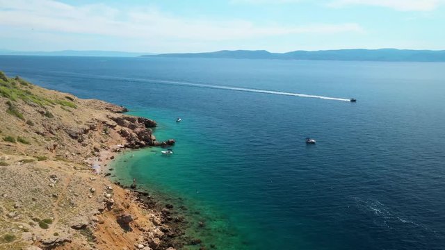 Middle angle aerial drone footage of a coastline in a bay in Vruja, Croatia. Pristine  teal, emerald/ turquoise water. Camera is following one boat that is arriving in the bay.