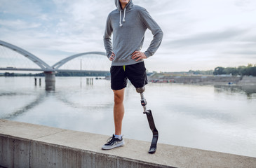 Fit healthy Caucasian handicapped man in sportswear and with artificial leg standing on quay with...