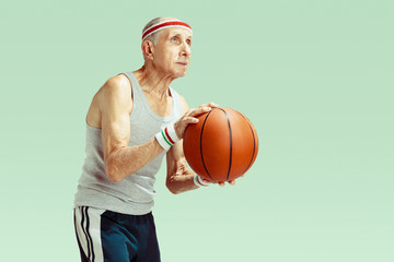 Naklejka premium Senior man wearing sportwear playing basketball isolated on green background. Caucasian man in great shape stays active and sportive. Concept of sport, activity, movement, wellbeing. Copyspace, ad.