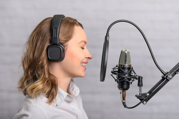 Female vocal recording. Young girl with microphone and headphones in recording studio. Recording of...