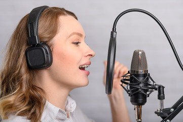 Female vocal recording. Young girl with microphone and headphones in recording studio. Recording of vocal, blogger, reading text, voice acting.