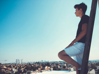 Young attractive man posing in front of camera on the roof of a residential building standing on a ladder