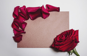 Brown kraft paper under rose petals and big gorgeous red rose bud. Romantic card mockup with copy space.