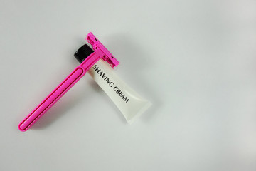 Pink shaving stick and white tube with shaving cream on light background with shadows. Woman body care concept closeup image with copy space