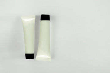 Two blank white tubes with black top caps on light background with shadows. Closeup mockup of cosmetics containers for cream, paste, lotion, gel, shampoo and others