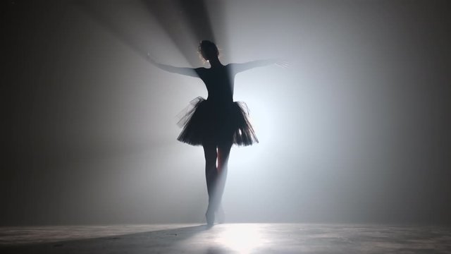 Solo performance by ballerina in tutu dress against backdrop of luminous neon spotlight in theater. Silhouette of woman in pointe shoes dancing classical movements. 4k.