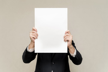 a man in a suit holds a white sheet in front of him. man hiding behind a poster. the man on the face of the white pattern copy space