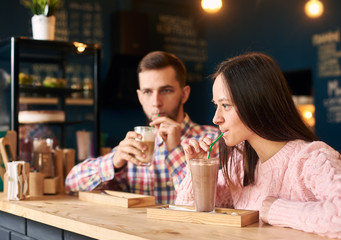 Young stylish happy couple sitting at cafe table, drinking coffee. Young man and woman at coffee shop. Romantic acquaintance concept. Focus on woman
