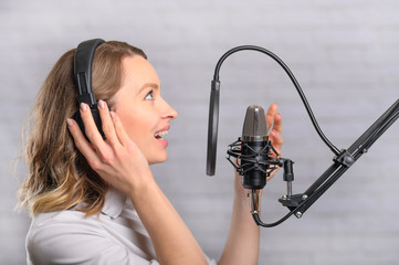 Female vocal recording. Young girl with microphone and headphones in recording studio. Recording of...