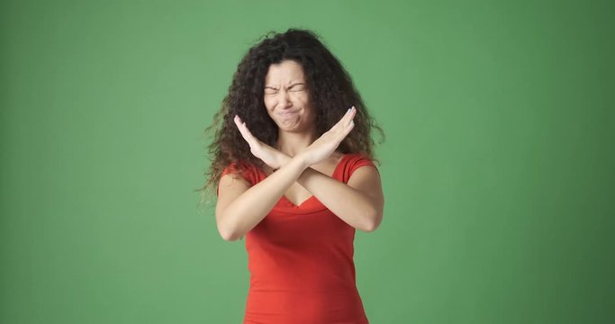 Serious young woman crossing her arms and saying no over green background