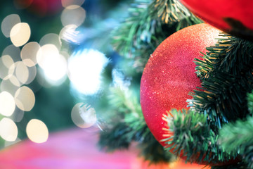 Closeup of red bauble hanging from a decorated christmas tree on blurred of  lights with decorated tree, sparkling and bokeh background. copy space for your text.