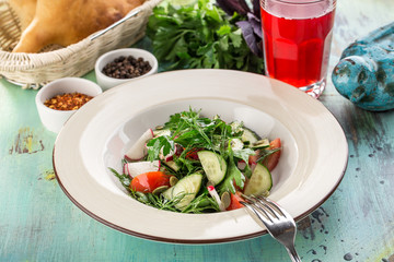Plate of healthy green garden salad with radish, tomato and cucumber on blue wooden table