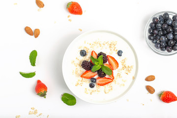 Greek yogurt with granola fresh strawberries, blueberries, blackberries and almonds on white table. Healthy snack. Breakfast food. Top view, copy space.