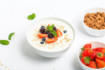 Greek yogurt with granola fresh strawberries, blueberries, blackberries and almonds on white table. Healthy snack. Breakfast food. 