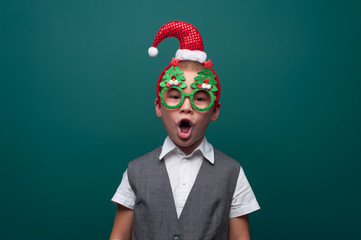 Adorable little boy in Christmas accessories posing on green wall