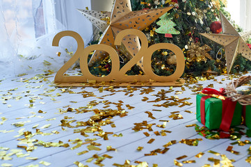 Meeting the new year 2020. Gold numbers on the background of the Christmas tree. Confetti on the floor.