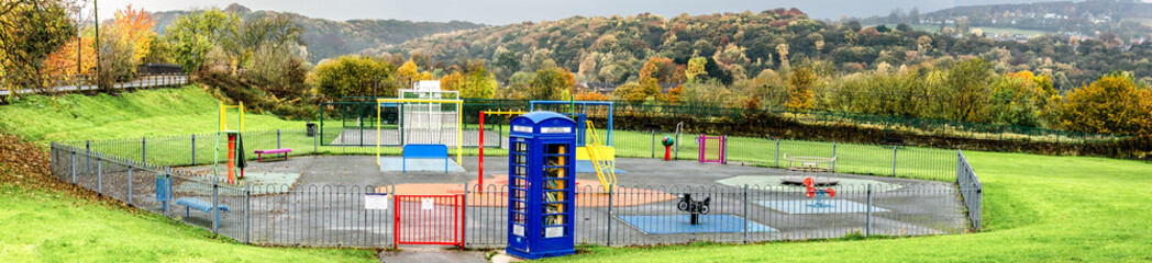 A panorama of a playground equipped with games, swings and slides and with a telephone box...