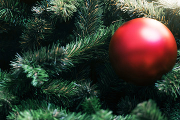 Closeup of red bauble hanging from a decorated christmas tree on blurred of  lights with decorated tree, sparkling and bokeh background. copy space for your text.