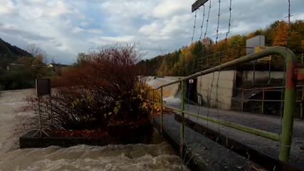 Slow motion left pan dirty rainfall water leaving small concrete canal and falling in river with plastic debris - Powered by Adobe