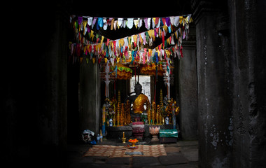 Buddha statue in the dark behind colorful flags in the temples of Angkor, Cambodia, south-east Asia.