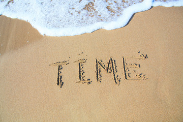 Word TIME drawn on the sand of sandy beach