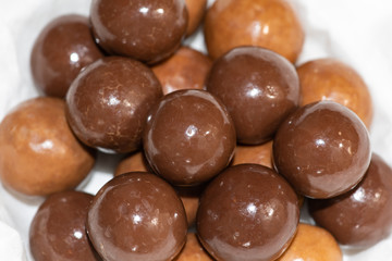 Dark and milk chocolate covered balls.  Malted milk balls on plate with white paper. Round candy caramel.  Selective focus.