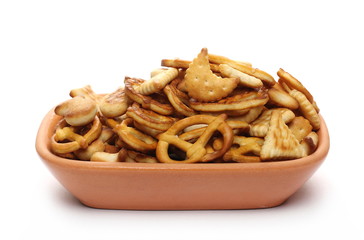 Salty cracker and pretzel snacks, party mix in clay bowl, pot isolated on white background