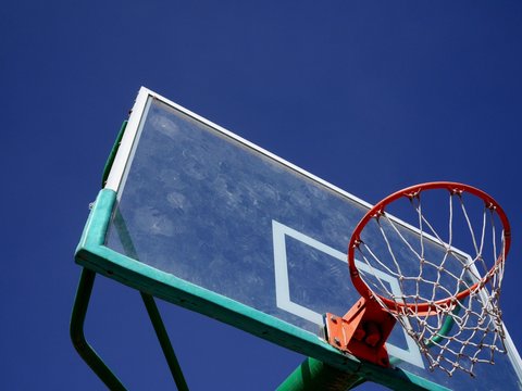 Photo of a basketball backboard and rim with net against blue sky. Basketball equipment for outdoor use.