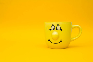 Smiley yellow ceramic cup on yellow background. Yellow mug empty blank for coffee or tea. Space for...