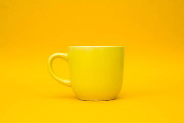 Yellow ceramic cup on yellow background. Yellow mug empty blank for coffee or tea. Space for text