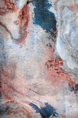 The surface of the wall made of natural stone with blue and red stains, scratches and traces of processing and polishing. Abstract, trendy, modern, texture background with copy space.