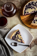 Blueberry pie on a wooden plate, a piece of blueberry pie on a white plate and a Cup of hot tea on a beautiful gray background